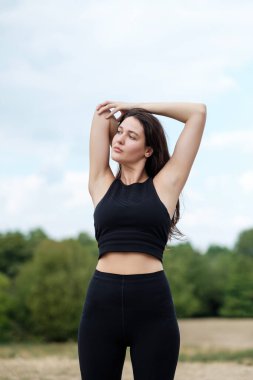 Genç beyaz bir kadın Londra 'da bir ormanda yoga yapıyor ve esniyor. Siyah yoga kıyafeti giyiyor...