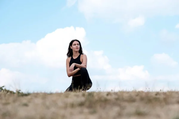 Young yoga caucasian woman is squat on the grass ready for doing yoga. She is wearing black yoga outfit.