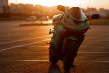 Tanımlanamayan stil sahibi, kasklı erkek motosikletçi, günbatımı gökyüzünün arka planında, park halindeki motosiklette oturuyor.