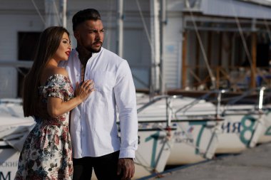 Moda kıyafetleri içinde sevgi dolu bir çift yazın teknelerle limanda beklerken kucaklaşıyorlar.