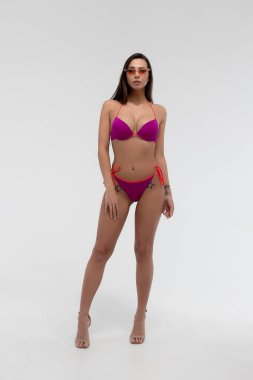 Mükemmel seksi vücudu olan, kırmızı bikini ve güneş gözlüğü takmış, beyaz arka planda duran zayıf, genç bir esmer.