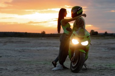 Birbirlerine aşık çiftin kumlu deniz kıyısında güneş batarken motosikletin yanında nazikçe kucaklaşmalarını yan görüyorum.