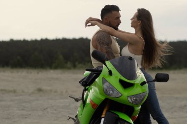 Birbirlerine aşık çiftin kumlu deniz kıyısında güneş batarken motosikletin yanında nazikçe kucaklaşmalarını yan görüyorum.