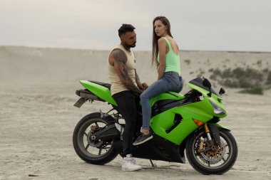 Yaz akşamları kumlu plaja park etmiş modern motosiklette oturan havalı genç çift.