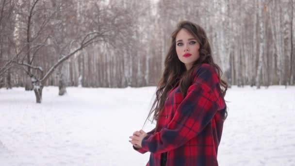 Молода жінка з хвилястим волоссям стоїть і торкається обличчя в зимовому лісі — стокове відео