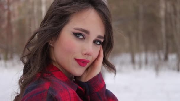Ung kvinna med vågigt hår stående och rörande ansikte i vinterskogen — Stockvideo