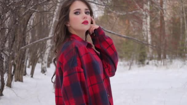 Νεαρή γυναίκα με κυματιστά μαλλιά στέκεται και συγκινητικό πρόσωπο στο δάσος του χειμώνα — Αρχείο Βίντεο
