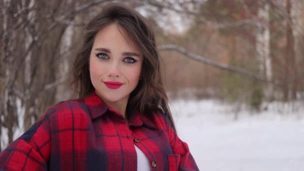 Mladá žena s vlnitými vlasy stojící a dotýkající se obličeje v zimním lese — Stock video