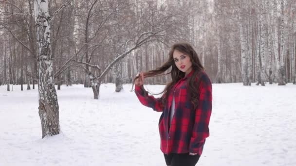 在冬季的森林里，一位留着波浪般的头发、面庞的年轻女子站在那里 — 图库视频影像
