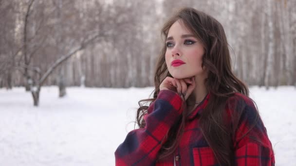 Mladá žena s vlnitými vlasy stojící a dotýkající se obličeje v zimním lese — Stock video