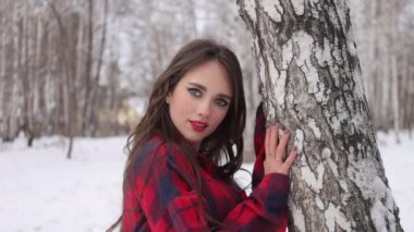 Kış ormanında dalgalı saçlı genç bir kadın ayakta duruyor ve yüzüne dokunuyor.