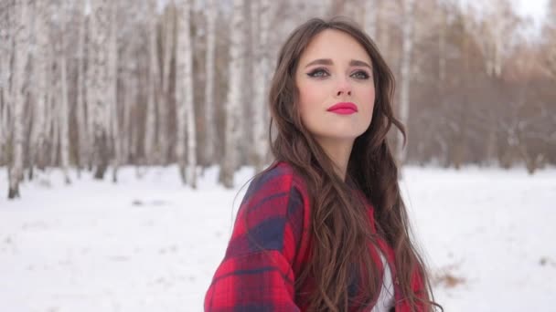 Νεαρή γυναίκα με κυματιστά μαλλιά στέκεται και συγκινητικό πρόσωπο στο δάσος του χειμώνα — Αρχείο Βίντεο