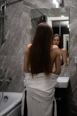 Banyoda aynanın önünde duran çıplak göğüslü zarif ve seksi bir kadın.