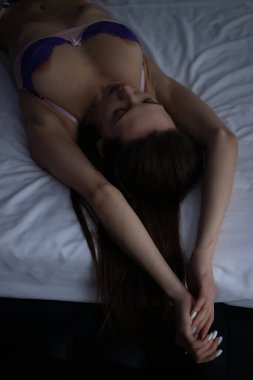 Yüksek açılı, dantel iç çamaşırlı, yatak odasındaki rahat yatağa uzanmış, gözleri kapalı bir kadın.