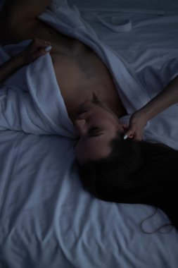 Üstsüz, bornozlu seksi bir kadın yatak odasında rahat bir yatakta yatıyor.