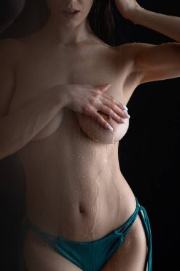 Meçhul, zayıf, ıslak vücutlu, uzun saçlı, çıplak göğsünü örten, siyah arka planda mavi külotlu bir kadın.