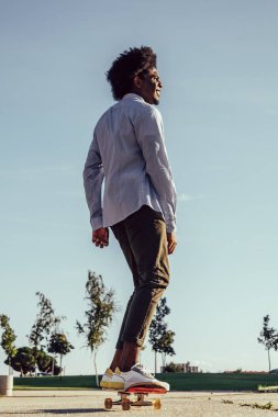 Güneş gözlüğü ve kaykay kap giyen genç koyu tenli adam resmini. Doğa arka planı.