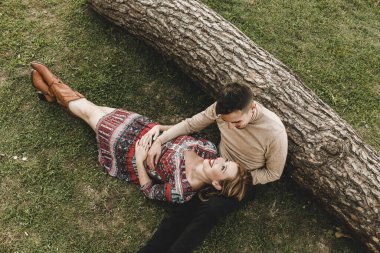 Bin yıllık bir çiftin ağaç gövdesine yaslanıp çimlerin üzerinde dinlenmesinin görüntüsü