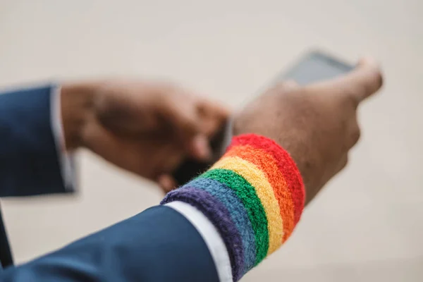 Zbliżenie ciemnoskórych dłoni za pomocą smartfona i bransoletki LGBT na zewnątrz. Kultura LGBTQIA. — Zdjęcie stockowe