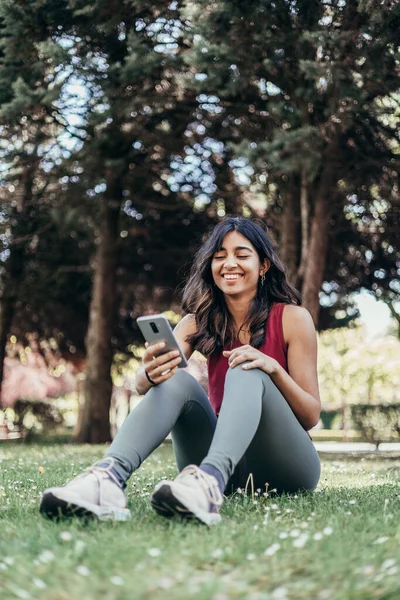 Beautiful indian ethnicity young woman using mobile phone sitting in park — Foto de Stock