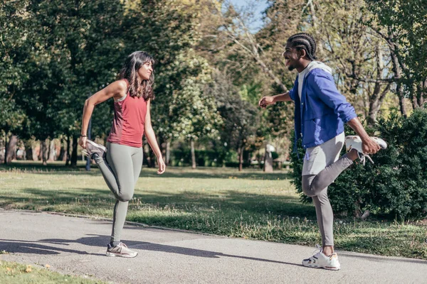 african american young man and indian young woman stretching together before running in park