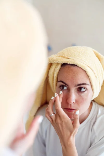 Happy z generation girl in towel after shower look in mirror apply moisturizing facial cream, morning beauty routine, skincare concept