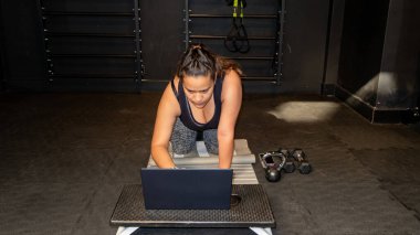 Beden eğitimi dersinde bilgisayarın önünde diz çöken genç bir kadın çevrimiçi sınıfa hazırlanıyor.