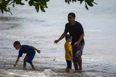 Sorong, Batı Papua, Endonezya, 12 Aralık 2021. Bir baba plajda oynayan çocuğuna eşlik eder.