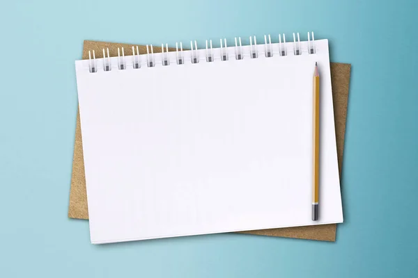 白いノートと鉛筆が青い紙の表面に置かれています ノートのコンセプト — ストック写真