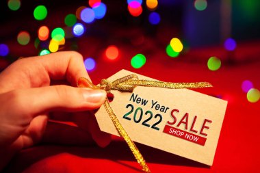 Bir kadının elinde yazılı bir etiket var - Yeni yıl indirimi 2022, hemen şimdi. Kırmızı arka planda, çok renkli bir sardalya..
