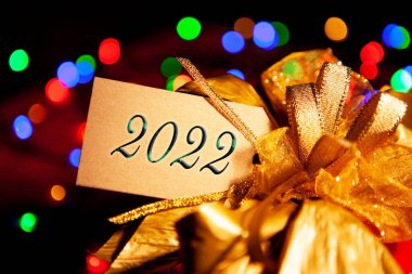 Altından bir fiyonklu hediye kutusunda 2022 yazılıydı. Çok renkli çelenk ışıklarıyla şenlikli bir arka plandaydı. Kaplanlı tebrik kartı, yılbaşı ve yeni yıl konsepti..