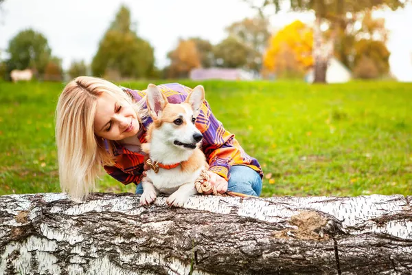 Portrait of a woman with a dog corgi breed. A beautiful blonde woman looks at her beloved pet, on a natural background of green grass in the park. The concept of an active lifestyle with a pet.