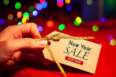 Bir kadının elinde yazılı bir etiket var. Yeni yıl indirimi, hemen şimdi. Kırmızı arka planda, çok renkli bir sardalya..