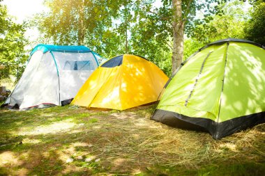 Ormanda mavi, sarı ve yeşil olmak üzere üç turist çadırı, turist kampında gün doğumu. Aktif yaz tatilleri, aile maceraları. Eko-turizm, sosyal mesafe. Boşluğu kopyala. 