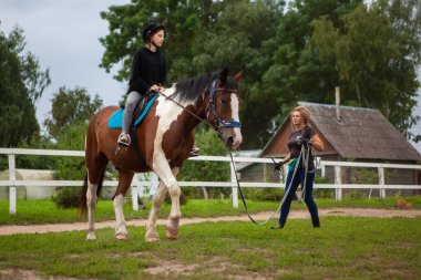 Belarus, Vitebsk region, July 9, 2021. Children's horse riding training, on the parade ground, on the horse ranch. In the foreground, a girl rider is practicing elements with a trainer.