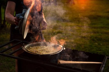 Bir kadın aşçı, pilav ya da tencere kapağını açar..