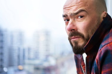 Pencerede sıradan giysiler içinde sakallı çekici kel bir adamın portresi, somurtkan, şaşkın ve hoşnutsuz bir şekilde kameraya bakıyor. Pencerenin dışında büyük bir şehrin bulanık bir manzarası var..