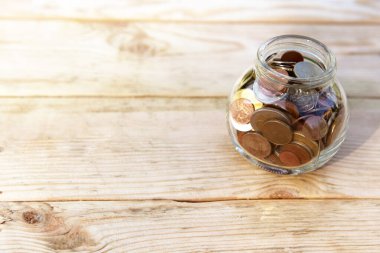 Bozuk paralarla dolu cam kavanoz ve ahşap bir arka planda bitki. Finans ve yatırım kavramı. 