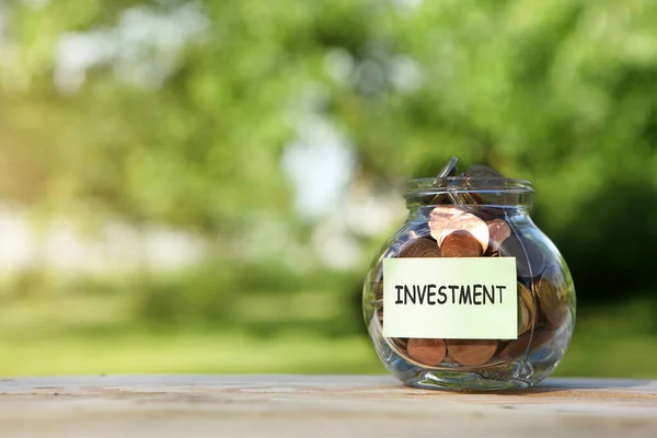 Investimento. Frasco de vidro com moedas, sobre uma mesa de madeira, sobre um fundo natural. — Fotografia de Stock
