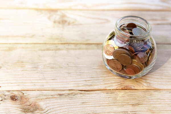 Glass jar with coins and a plant, on a wooden background. Finance and investment concept. 