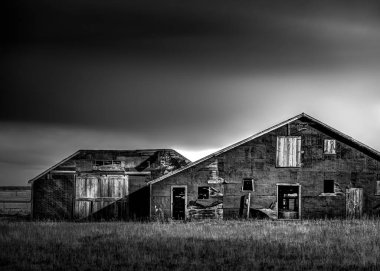 Ürkütücü eski bir ahırın siyah beyaz sahnesi. Gökyüzü karanlık ve uğursuz. Kapılar ve pencereler çok karanlık bir iç mekan gösteriyor.. 