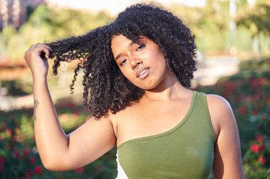 Genç bir kadın kıvırcık saçlarını eliyle çekiyor.