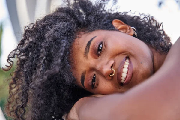 close up of young latina with curly hair and piercing smiling looking at the camera
