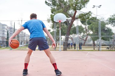 Basketbolcu basket atmadan önce topu sürüyor. Genç adam top ve spor kıyafetleri ile.