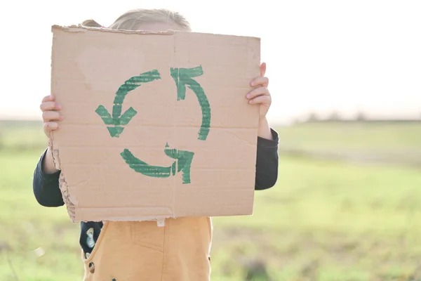 Girl\'s hand holding cardboard sign with recycling symbol