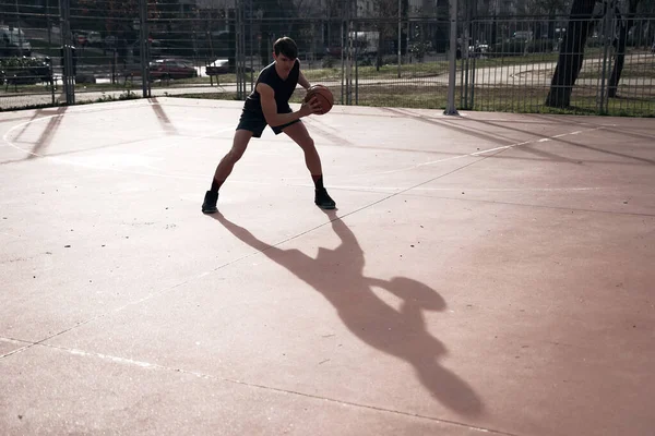 Sokakta uzun gölgeli basketbol oynayan genç adam.