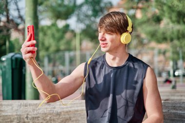 Neşeli genç sporcu akıllı telefonuyla kulaklıkla video görüşmesi yapıyor. Genç, formda bir erkek egzersiz yaptıktan sonra selfie çekiyor.