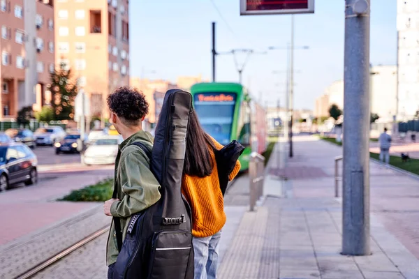 Tren ya da tramvay bekleyen genç bir çiftin arkasından manzara. İki müzisyen, birinin sırtında gitar ve ukuleleli bir kadın..