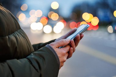 Şehir sokaklarında gece akıllı telefon kullanan bir kadının ellerinin yakın plan görüntüsü, arama veya sosyal ağ konsepti,