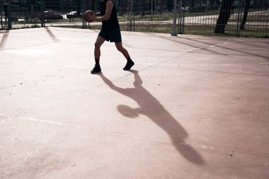 Sokakta uzun gölgeli basketbol oynayan genç adam.